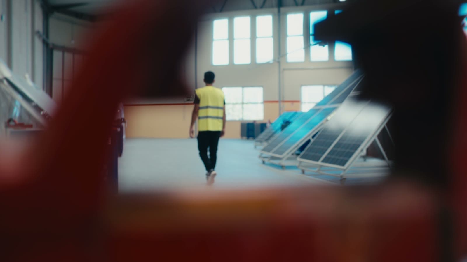 Pessoa de colete amarelo a caminhar para os painéis solares, vista através de uma máquina