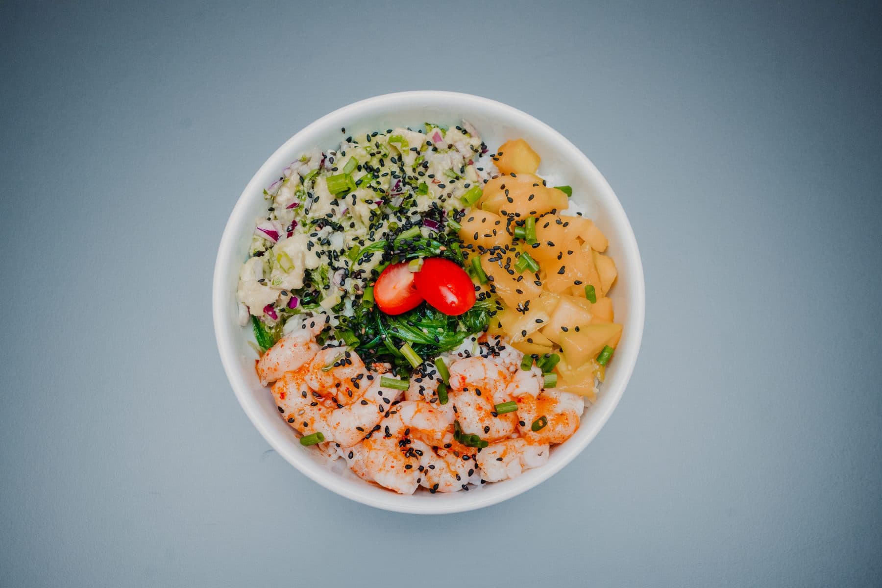 Taça de poke de camarão vista de cima, com sésamo preto, algas e tomate cereja