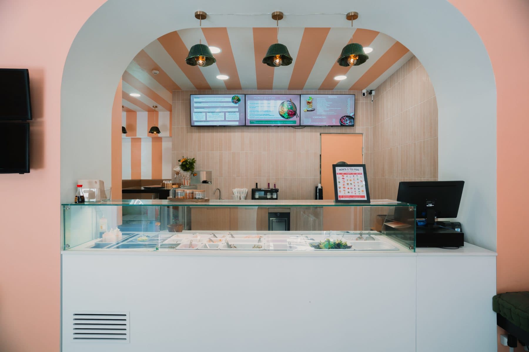 Balcão de vidro por baixo de um arco, com os ecrãs do menu na parede ao fundo, no Ohana Poke