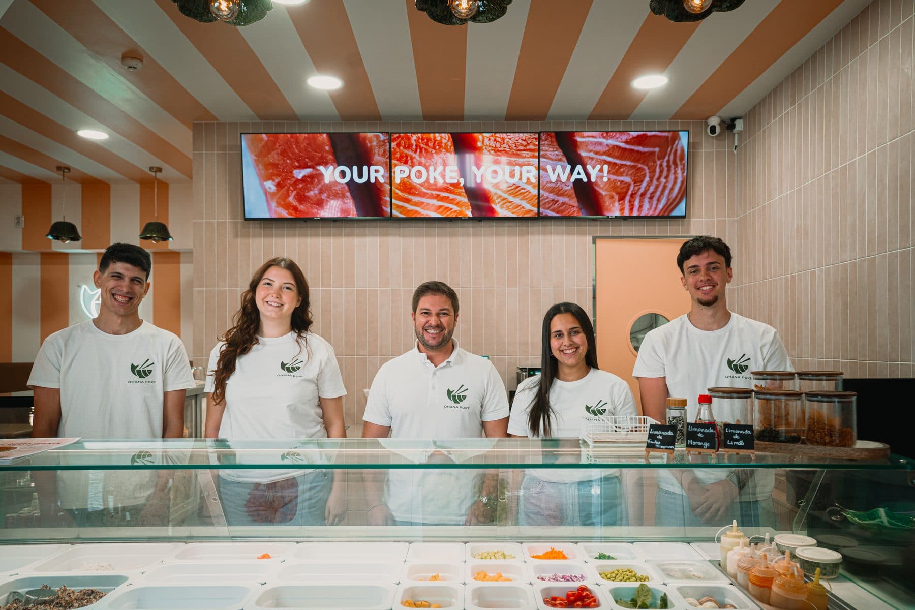 A equipa do Ohana Poke, cinco pessoas de branco com o logótipo, atrás do balcão dos ingredientes