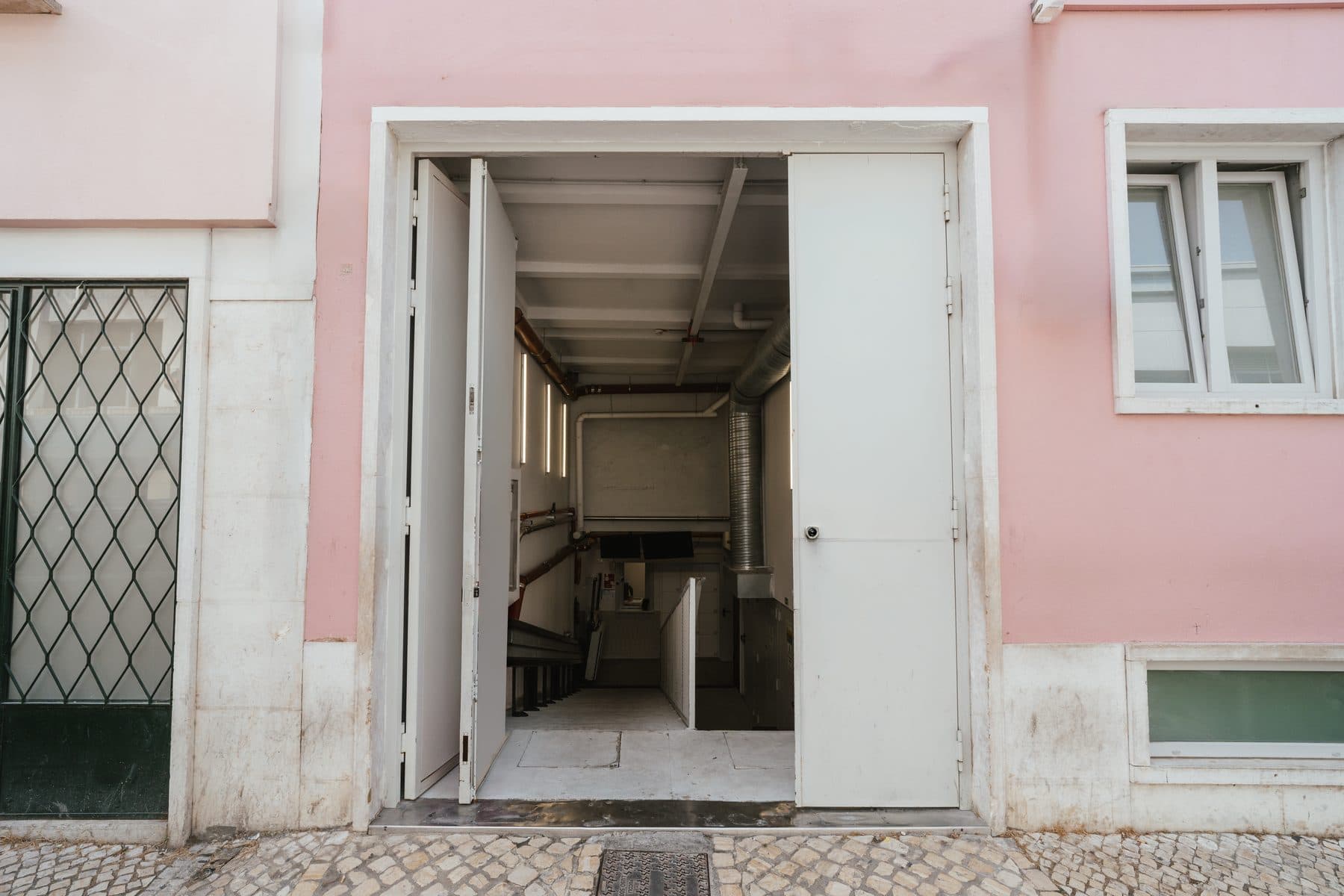 Porta dupla aberta numa fachada cor-de-rosa, com o interior do edifício da ProKitchens ao fundo
