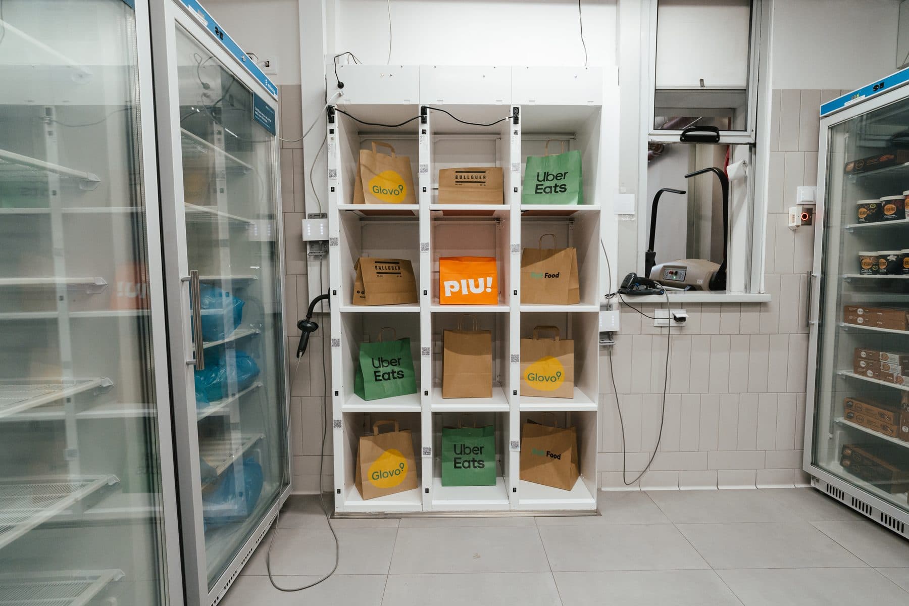 Sacos de entrega prontos a levantar, nas prateleiras entre dois frigoríficos