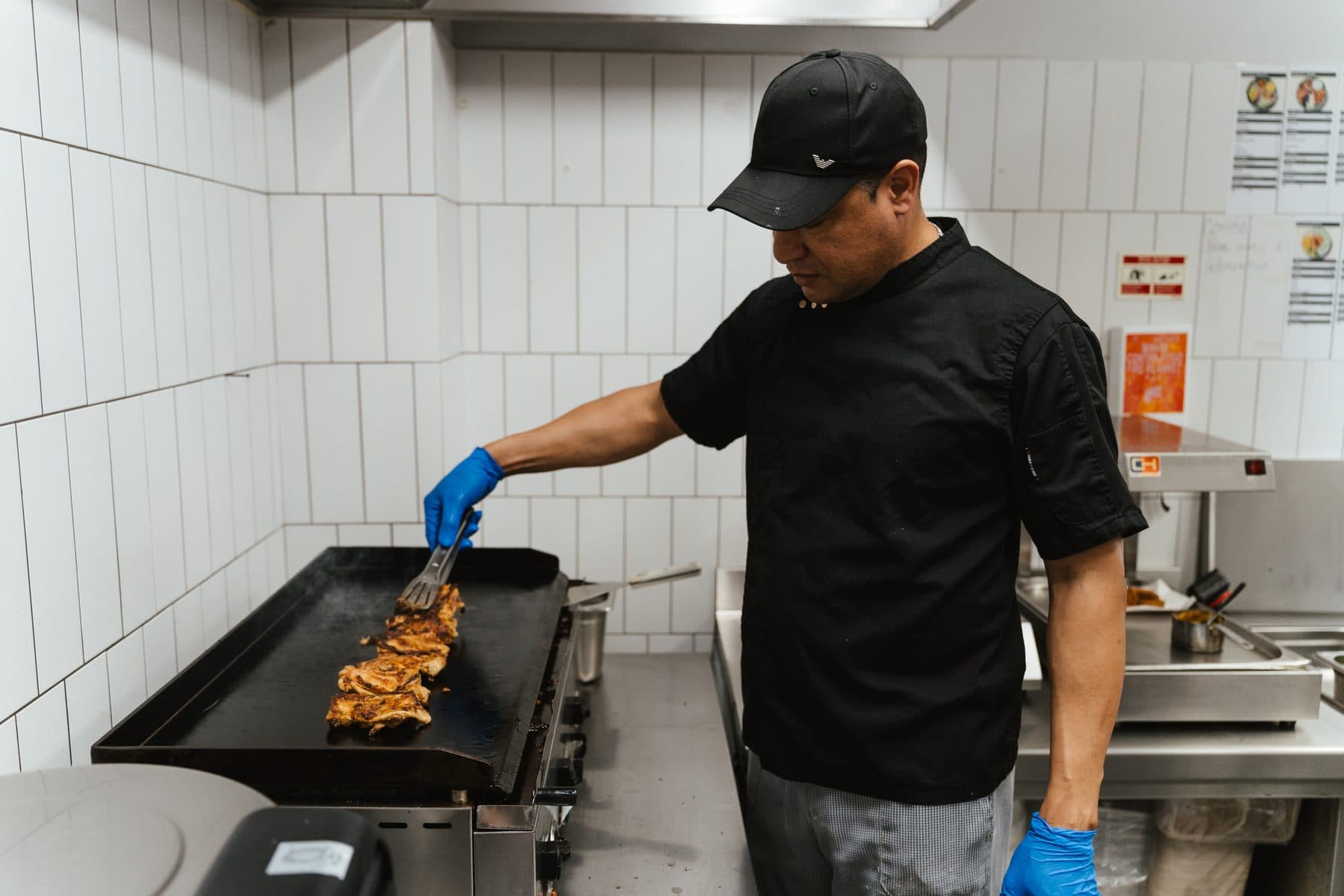 Cozinheiro de boné a virar frango na chapa, numa das cozinhas