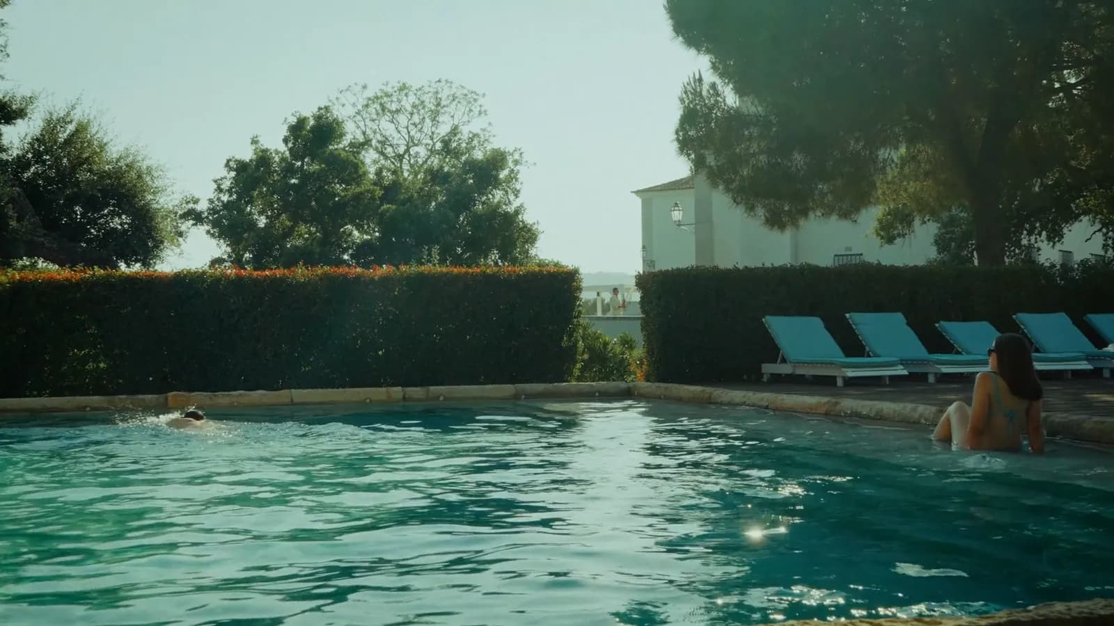 Hóspede sentada à beira da piscina do Hotel Casa Palmela, com as espreguiçadeiras ao fundo