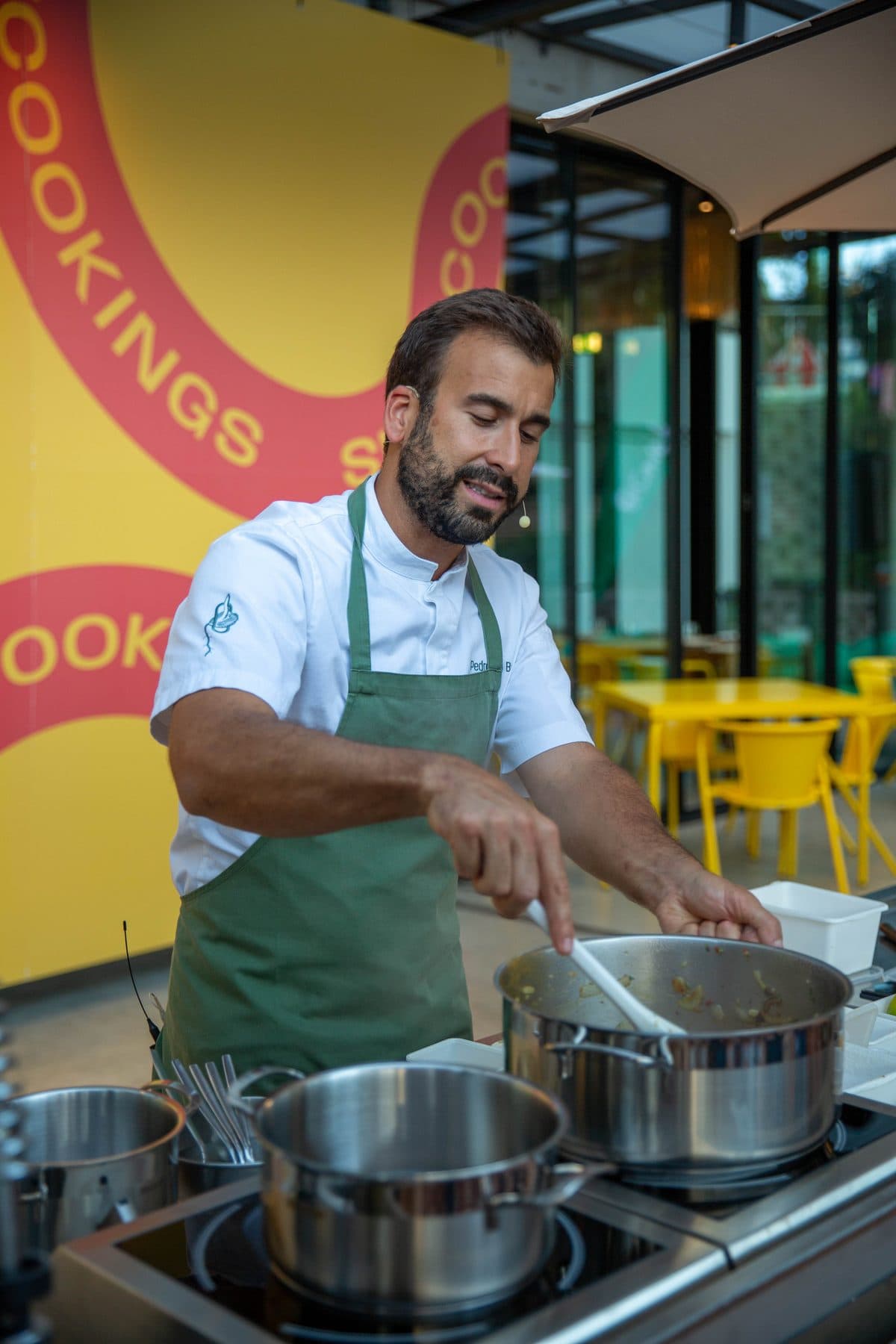 Cozinheiro de avental verde a mexer um tacho no palco dos showcookings