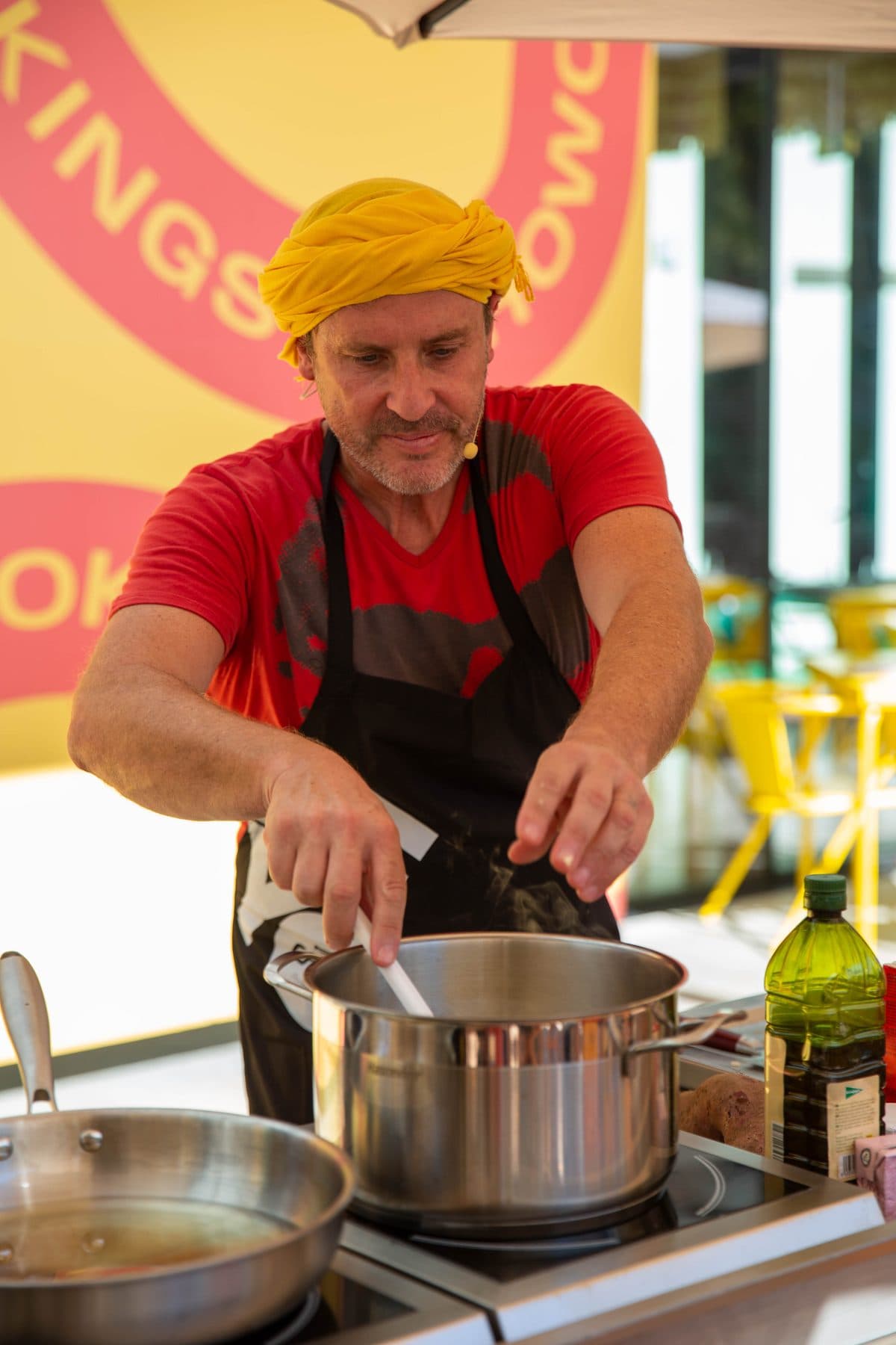 Cozinheiro de turbante amarelo e avental a cozinhar num tacho no palco dos showcookings