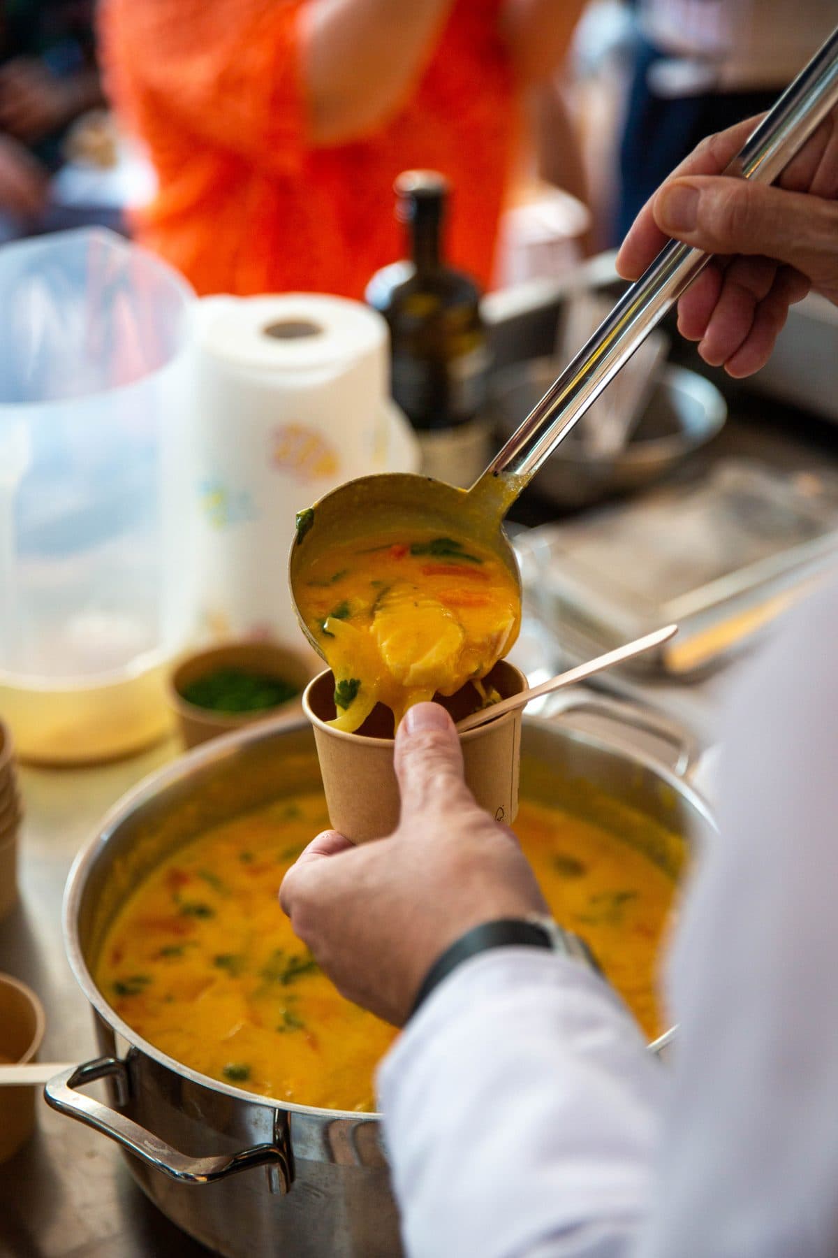 Concha a encher um copo de papel com um caldo amarelo com legumes, por cima do tacho
