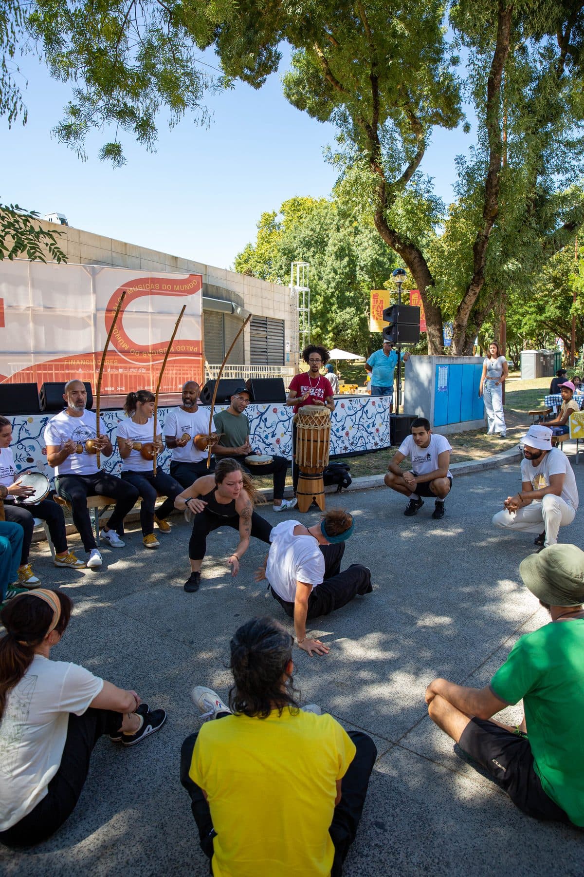 Roda de capoeira no parque, com dois jogadores ao centro e os músicos com berimbaus atrás