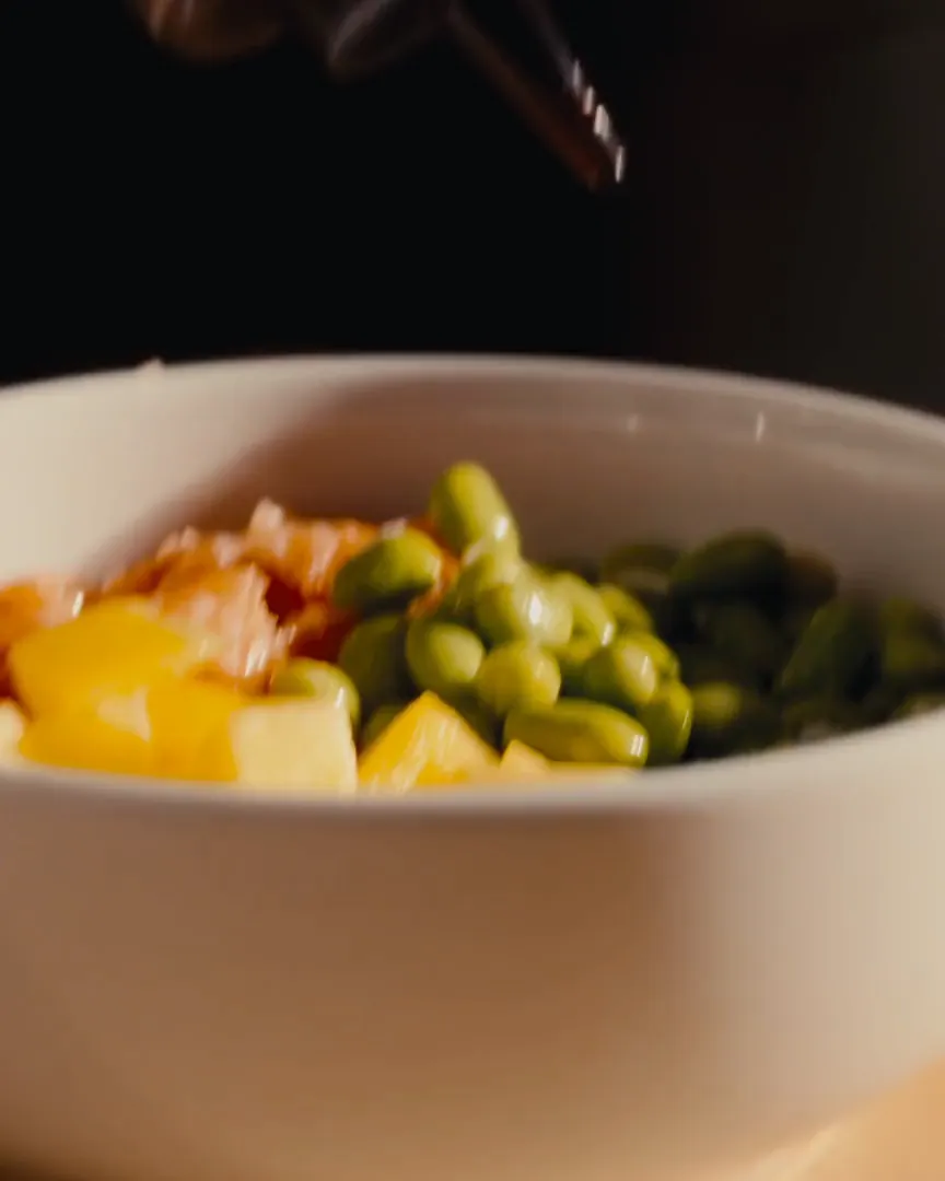 Sauce poured over a poke bowl with salmon and edamame, in a video Beyond Focus made for Ohana Poke