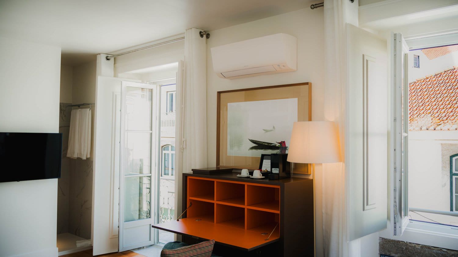 An orange desk by a window open onto the rooftops of Lisbon